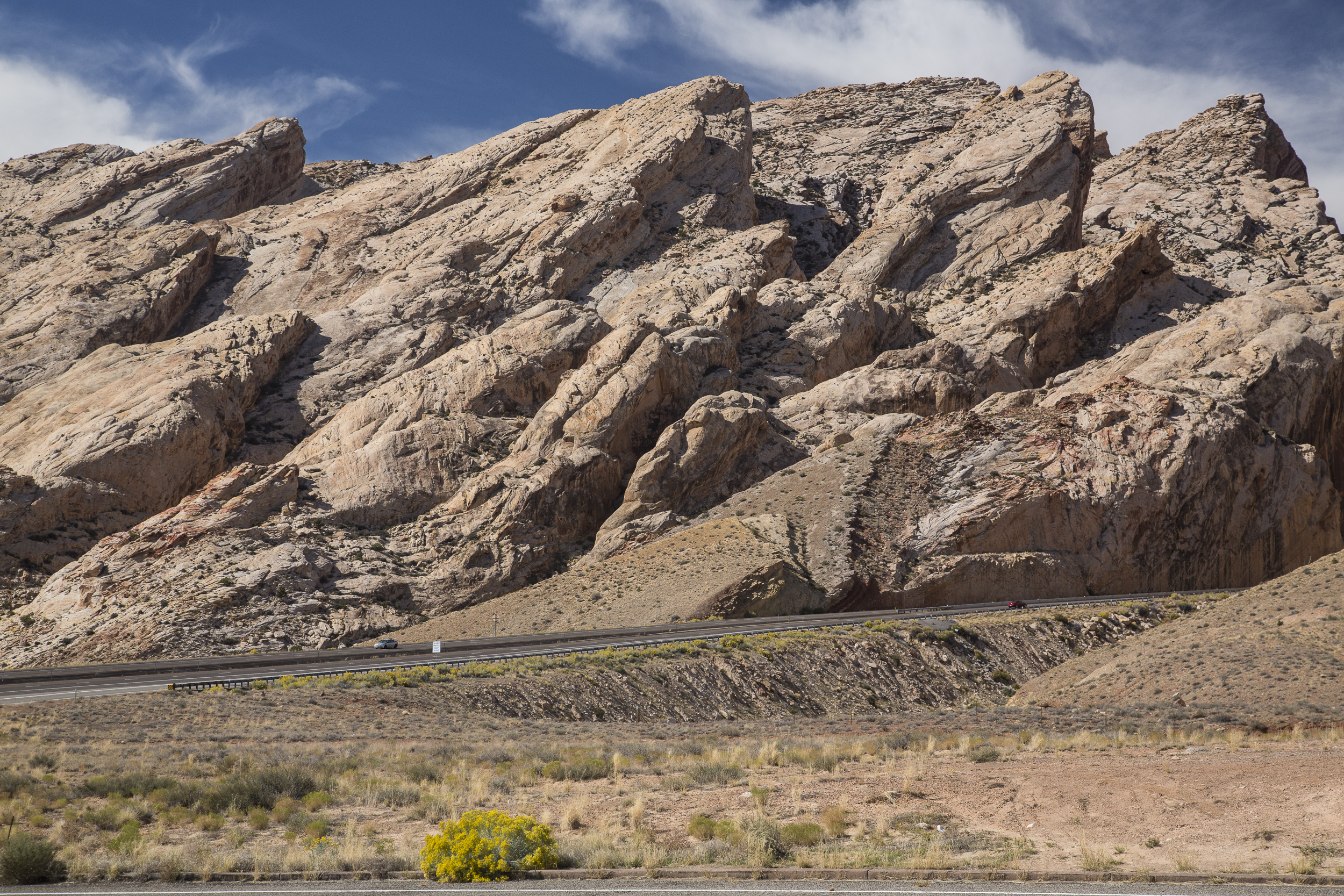 Steeply tilted sandstone strata of the San Rafael Reef rising above Interstate 70, with the highway visible at the base for scale