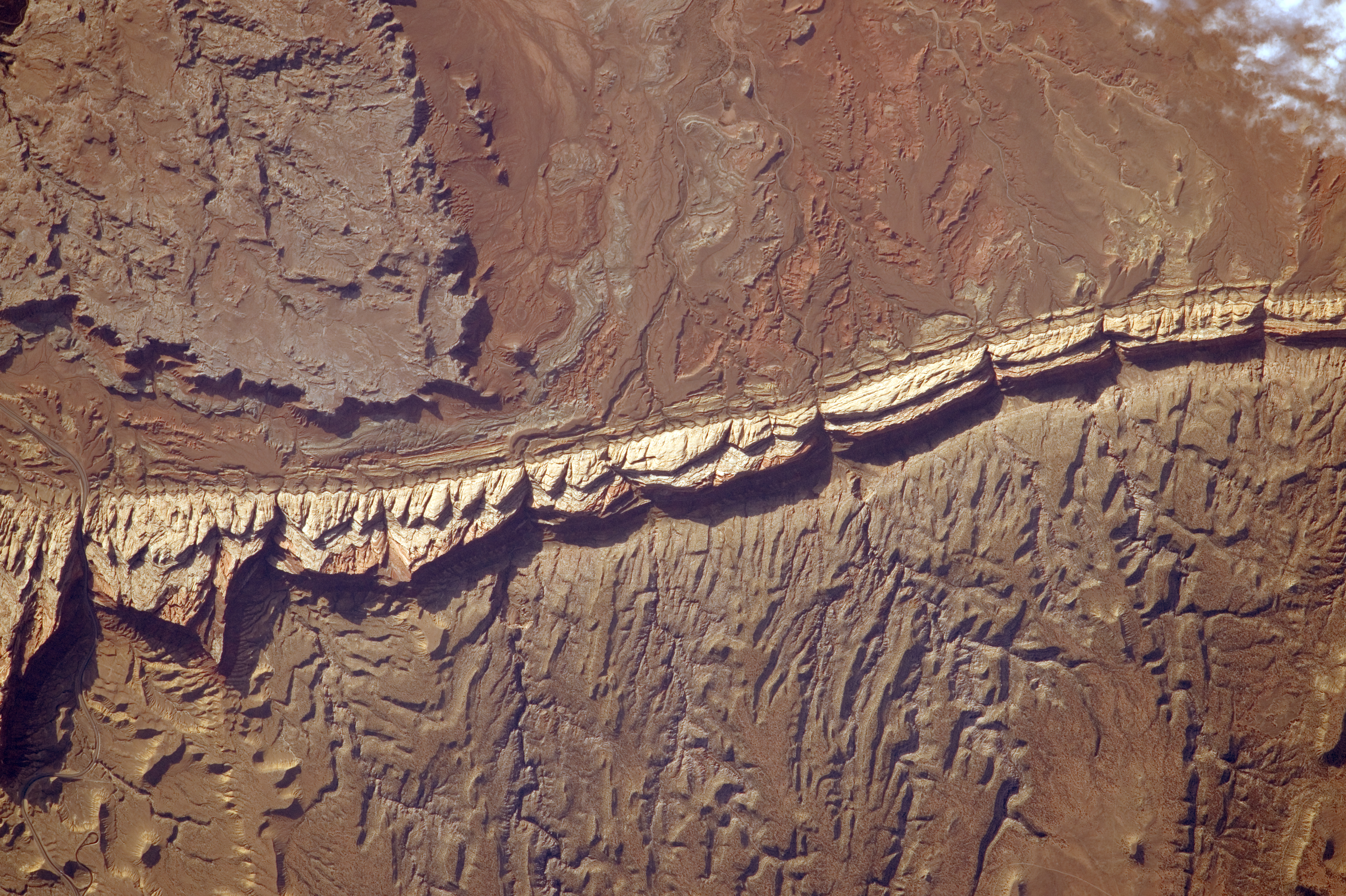 Oblique aerial photograph of the San Rafael Reef from the International Space Station, showing a continuous tilted hogback ridge fronting dissected desert canyons